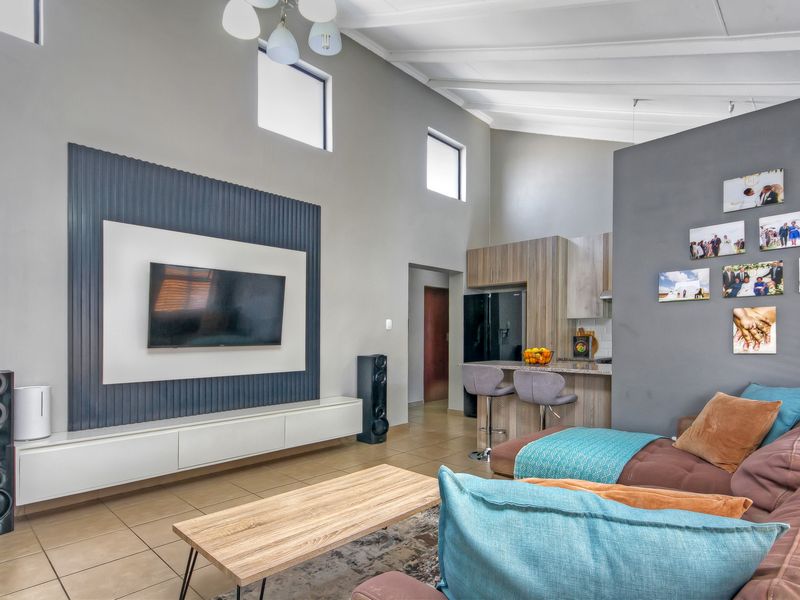 Spacious open-plan living area featuring a modern media wall, vaulted ceilings, and a functional kitchen with stone countertops and ample cabinetry.