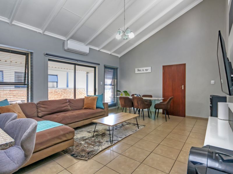 Spacious open-plan living and dining area featuring vaulted ceilings, tiled flooring, and direct access to the outdoor patio through sliding glass doors.
