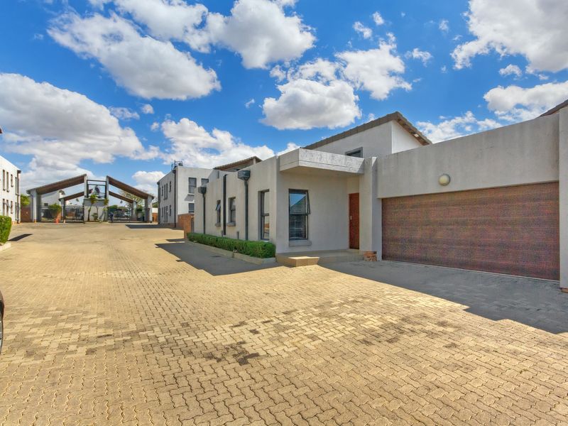 Front exterior view of the property featuring a paved driveway, double garage, and modern stucco facade within a secure complex.