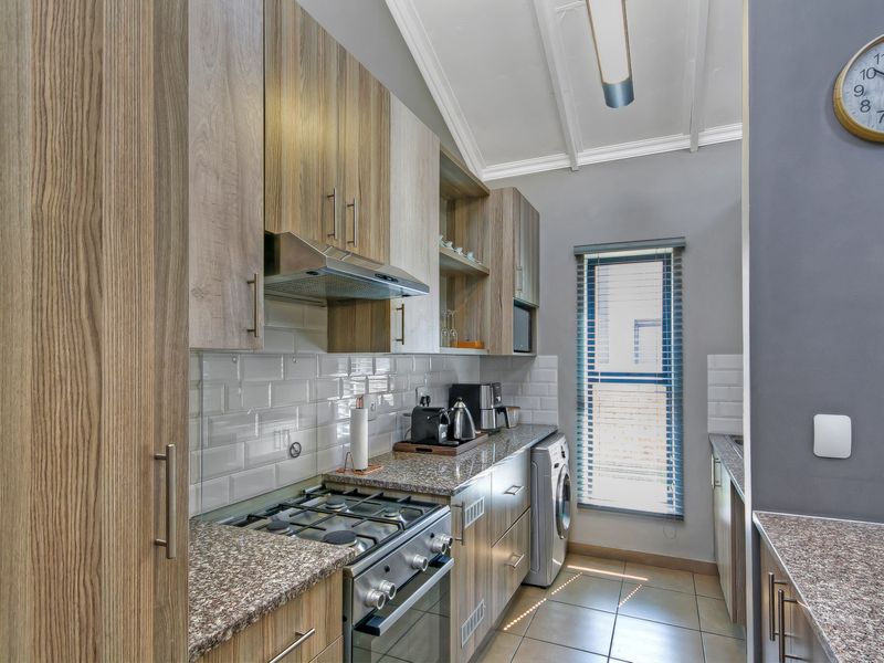 A well-appointed scullery featuring modern wood-finish cabinetry, granite countertops, a gas stove with extractor fan, and a subway tile backsplash.