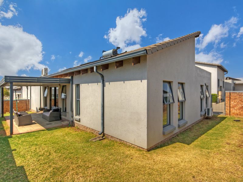Rear view of the property featuring a covered patio, landscaped garden, solar geyser, and modern aluminium window frames.