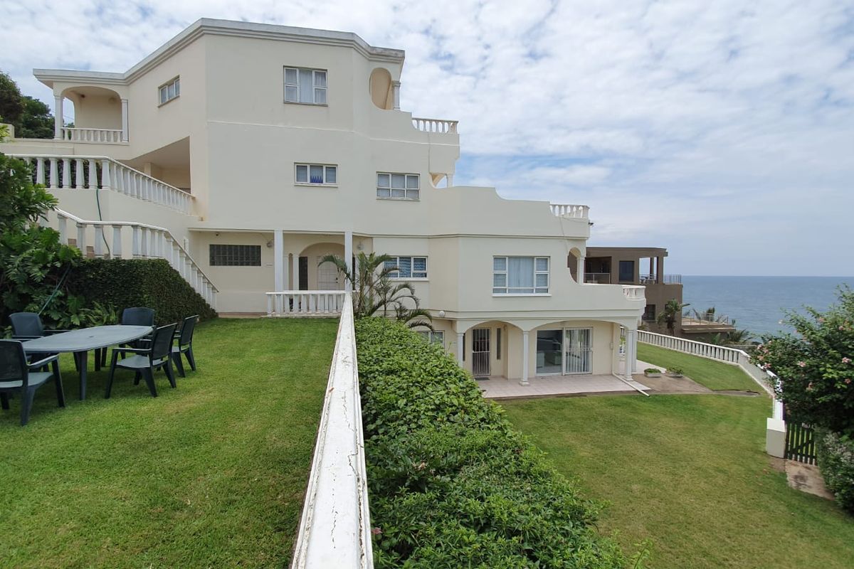 A multi-level rear exterior view of a coastal property featuring tiered lawns, balustrades, and direct ocean views.