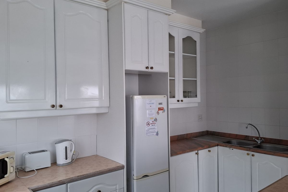 A functional kitchen featuring white cabinetry, laminate countertops, and a stainless steel sink with a tiled backsplash.