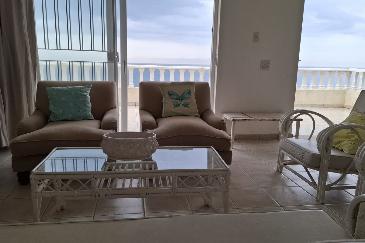 A bright living room featuring tiled floors and large sliding glass doors that open onto a balcony with ocean views.