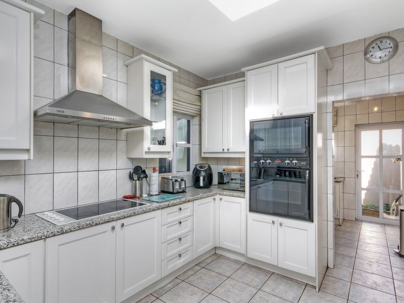 A well-maintained kitchen featuring white cabinetry, granite countertops, a built-in oven, electric hob, and a stainless steel extractor fan.