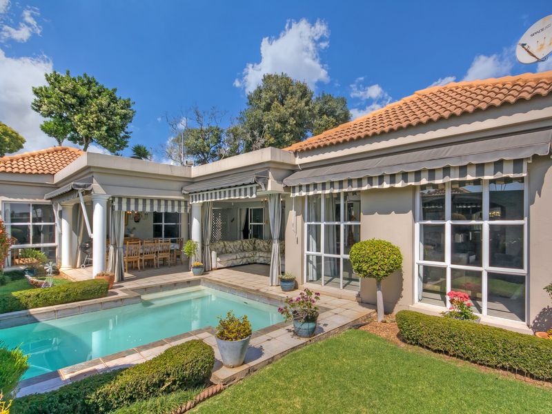 Rear exterior view featuring a swimming pool, covered patio area with retractable awnings, and well-maintained garden landscaping.