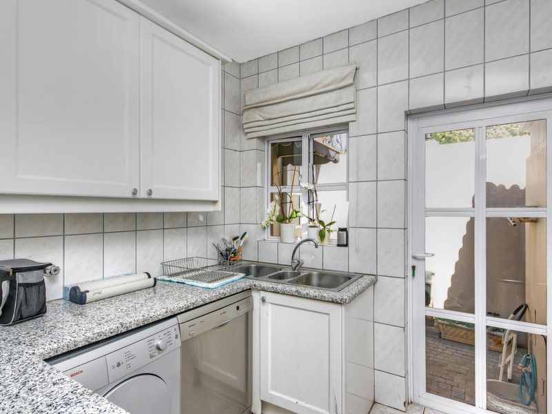 Functional laundry area featuring granite countertops, double stainless steel sink, built-in cabinetry, and direct access to the exterior.