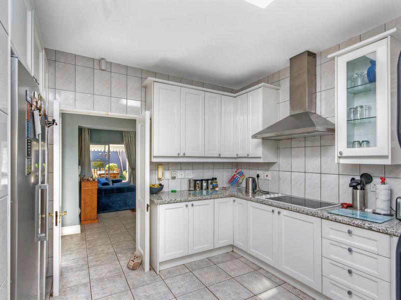 A functional kitchen featuring white cabinetry, granite countertops, a stainless steel extractor fan, and tiled finishes throughout.