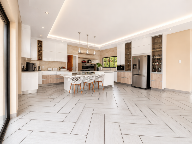 Modern open-plan kitchen featuring high-gloss cabinetry, a central island, integrated appliances, and elegant herringbone tile flooring with sophisticated recessed and cove lighting.
