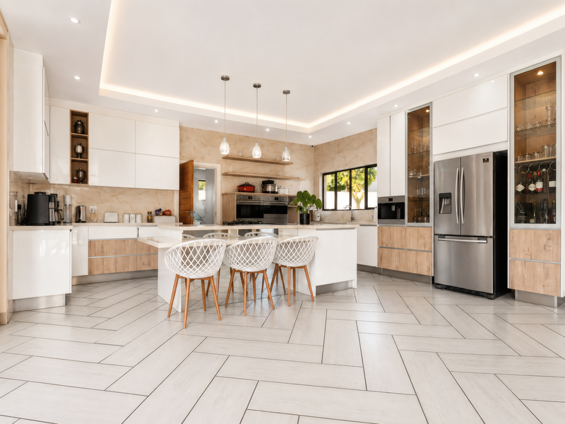 Modern, high-end kitchen featuring a central island, integrated appliances, sleek cabinetry, and elegant herringbone tile flooring with sophisticated recessed and cove lighting.