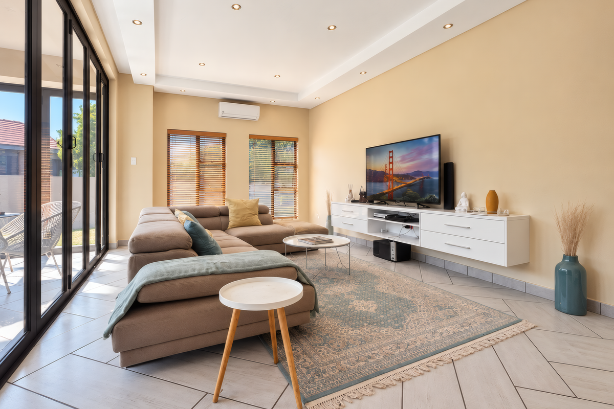 Spacious living room featuring tiled floors, recessed ceiling lighting, a wall-mounted media console, and large sliding glass doors providing access to the patio.