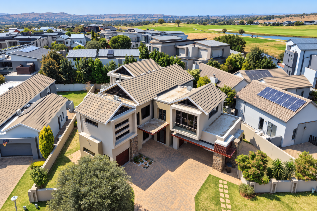 Aerial view of a modern residential property featuring a tiled roof, paved driveway, and solar panels, situated within a well-maintained estate.