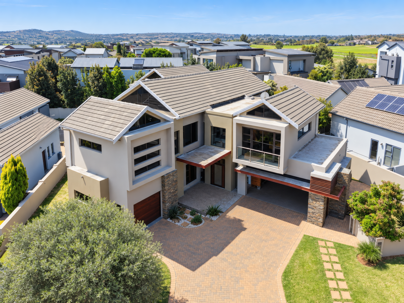 Aerial view of a modern double-story residential property featuring a paved driveway, double garage, stone accents, and a balcony in a suburban estate.