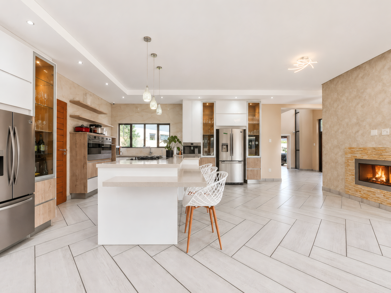 Modern open-plan kitchen and living area featuring a central island, high-end built-in appliances, stone feature wall with fireplace, and contemporary tiled flooring.