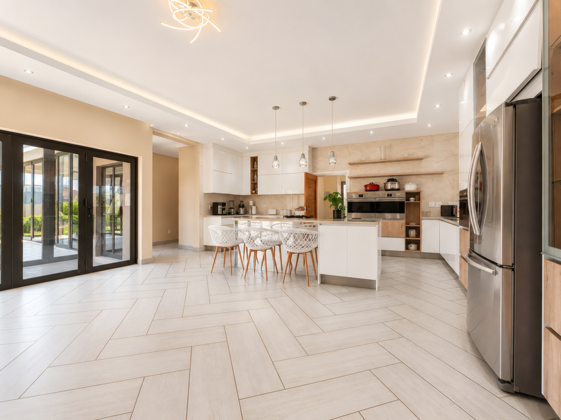 Modern open-plan kitchen featuring a central island, built-in appliances, herringbone tile flooring, and large glass sliding doors leading to the outdoor area.