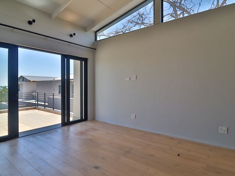 Bright, modern living area featuring timber flooring, exposed rafters, clerestory windows, and large sliding doors opening onto a private balcony.