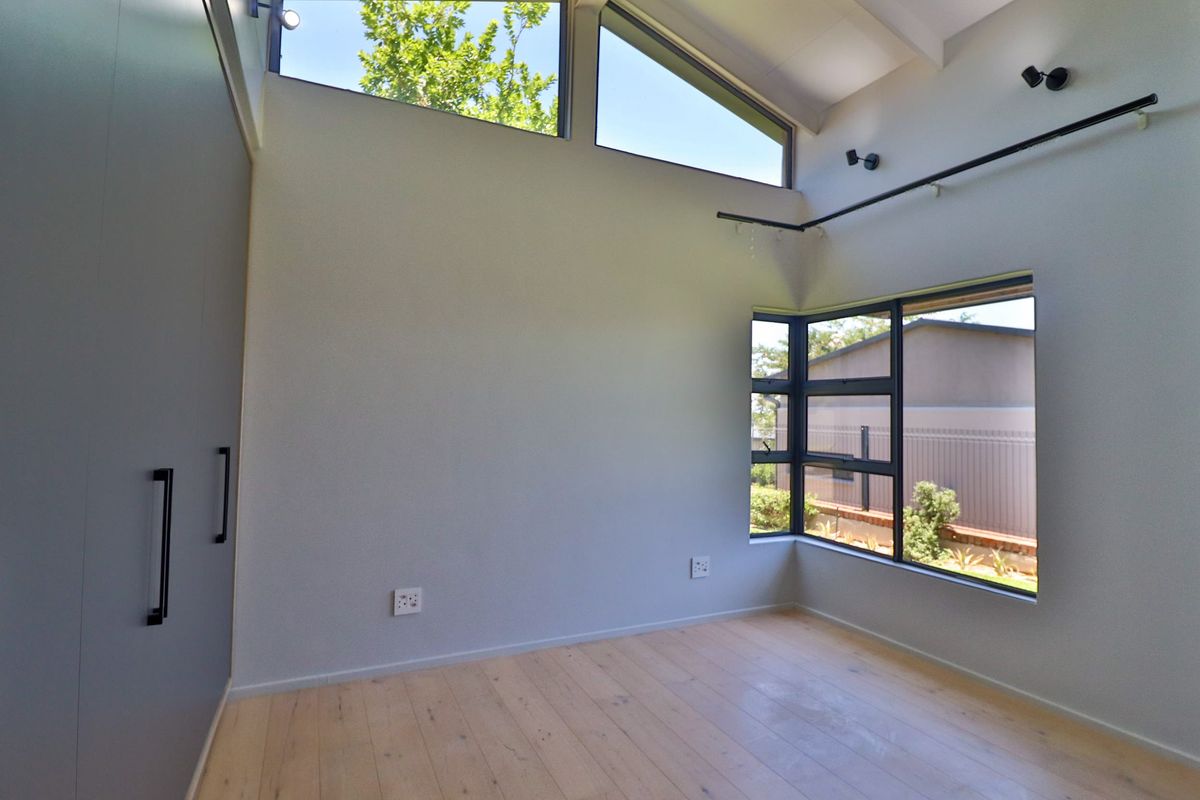 Bright and modern bedroom featuring timber flooring, built-in cupboards, raked ceilings with clerestory windows, and a corner window providing natural light.