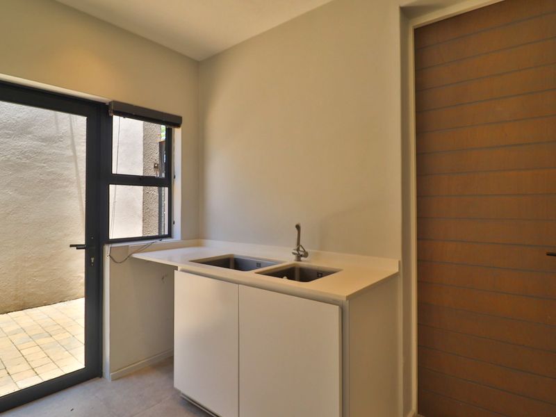 A clean, modern scullery featuring a double stainless steel sink, stone countertops, built-in cabinetry, and direct access to an outdoor area.