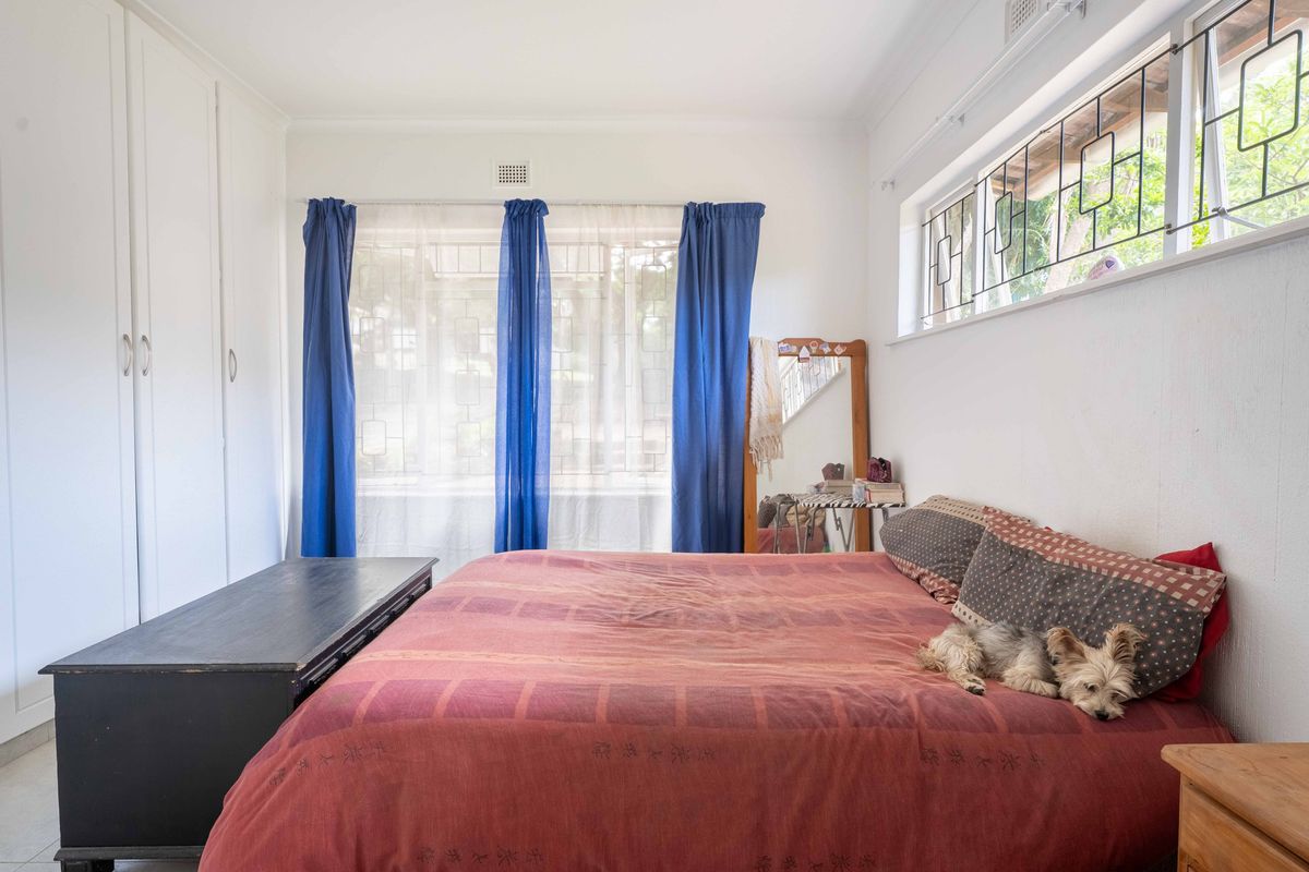 A bright bedroom featuring built-in wardrobes and windows fitted with security bars, offering a functional and well-lit living space.