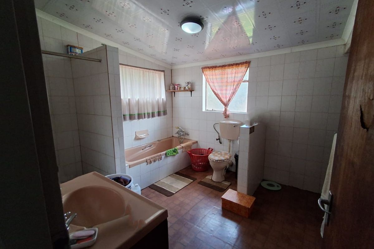 A dated bathroom featuring a built-in bathtub, pedestal basin, and toilet, with tiled walls and a patterned ceiling finish.
