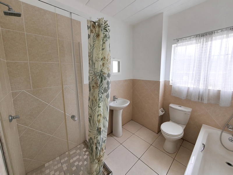 A functional bathroom featuring a separate shower enclosure, bathtub, pedestal basin, and toilet with neutral wall and floor tiling.
