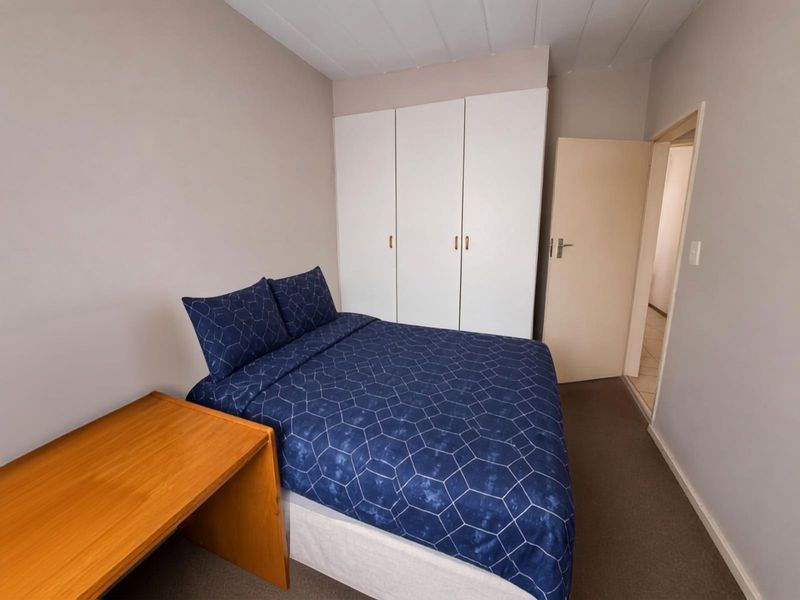 A functional bedroom featuring built-in cupboards, neutral wall finishes, carpeted flooring, and a panelled ceiling, providing a clean and practical living space.