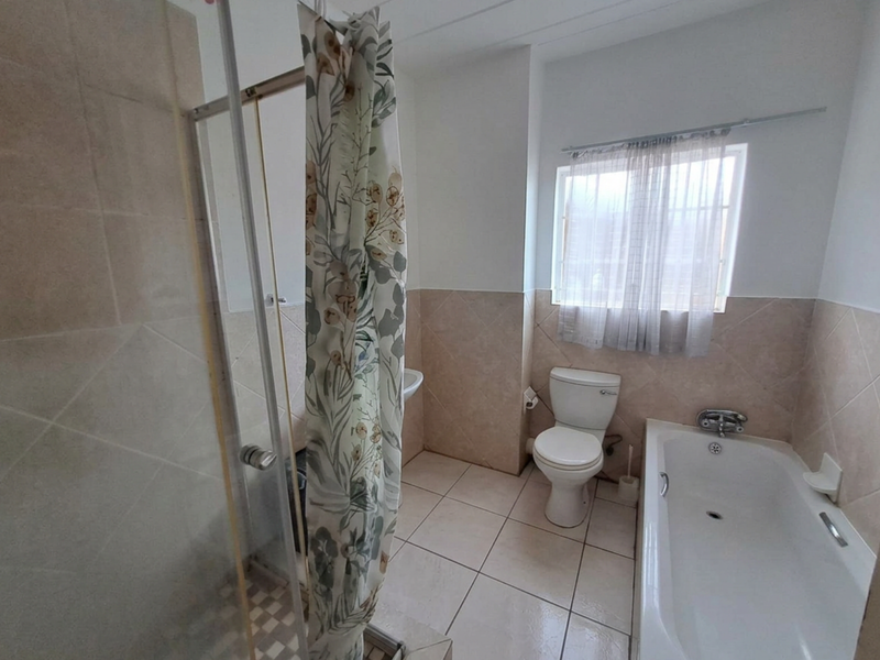 A functional bathroom featuring a shower enclosure, bathtub, toilet, and pedestal basin with neutral wall and floor tiling.
