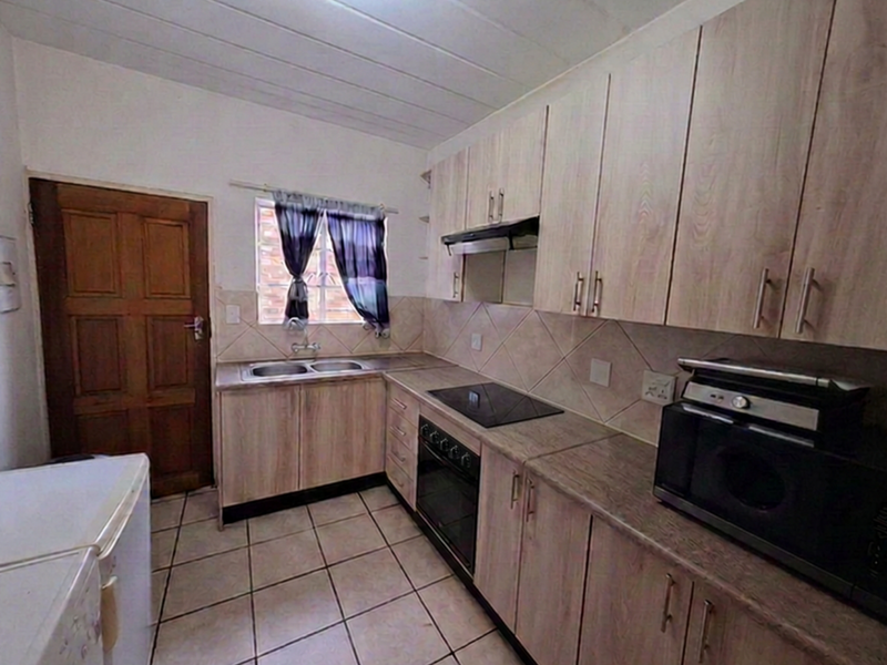 Functional kitchen featuring light wood-finish cabinetry, laminate countertops, built-in oven and hob, tiled backsplash, and tiled flooring.