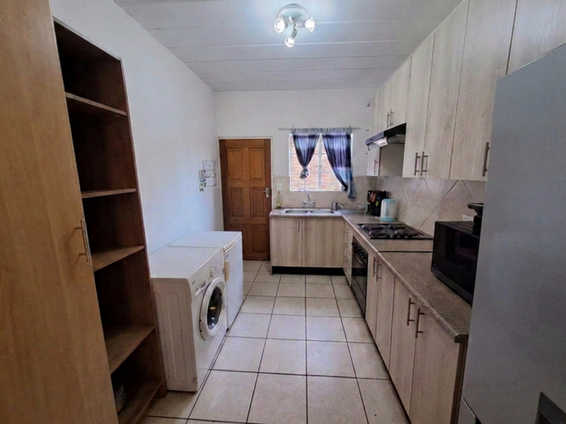 Functional kitchen featuring light wood-finish cabinetry, tiled flooring, built-in hob and oven, and a stainless steel sink with a window view.