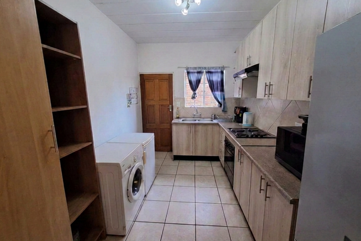 Functional kitchen featuring light wood-finish cabinetry, tiled flooring, built-in hob and oven, and a stainless steel sink with a window view.