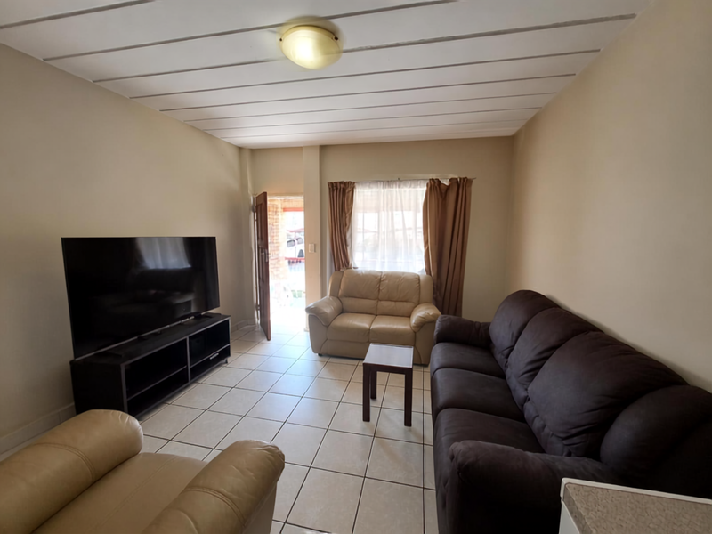 A living room featuring tiled flooring and a panelled ceiling, with direct access to the exterior through a doorway.