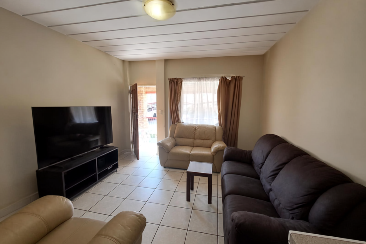 A living room featuring tiled flooring and a panelled ceiling, with direct access to the exterior through a doorway.