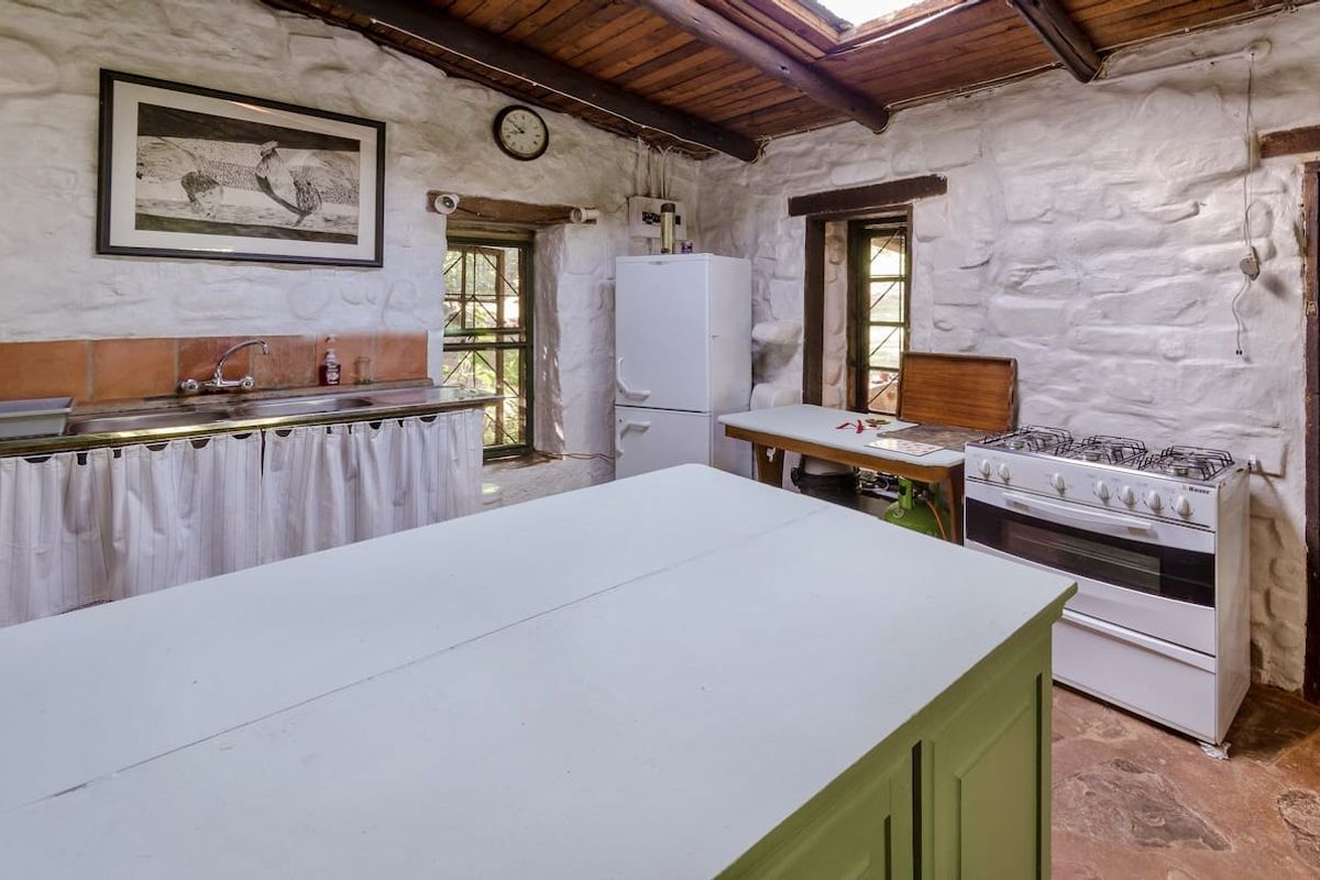 Rustic kitchen featuring exposed stone walls, timber beam ceiling, stone flooring, and a gas stove, offering a unique character-filled space.