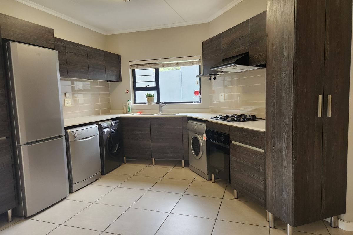 Modern kitchen featuring dark wood-grain cabinetry, light stone countertops, tiled flooring, and integrated stainless steel appliances including a gas hob and oven.