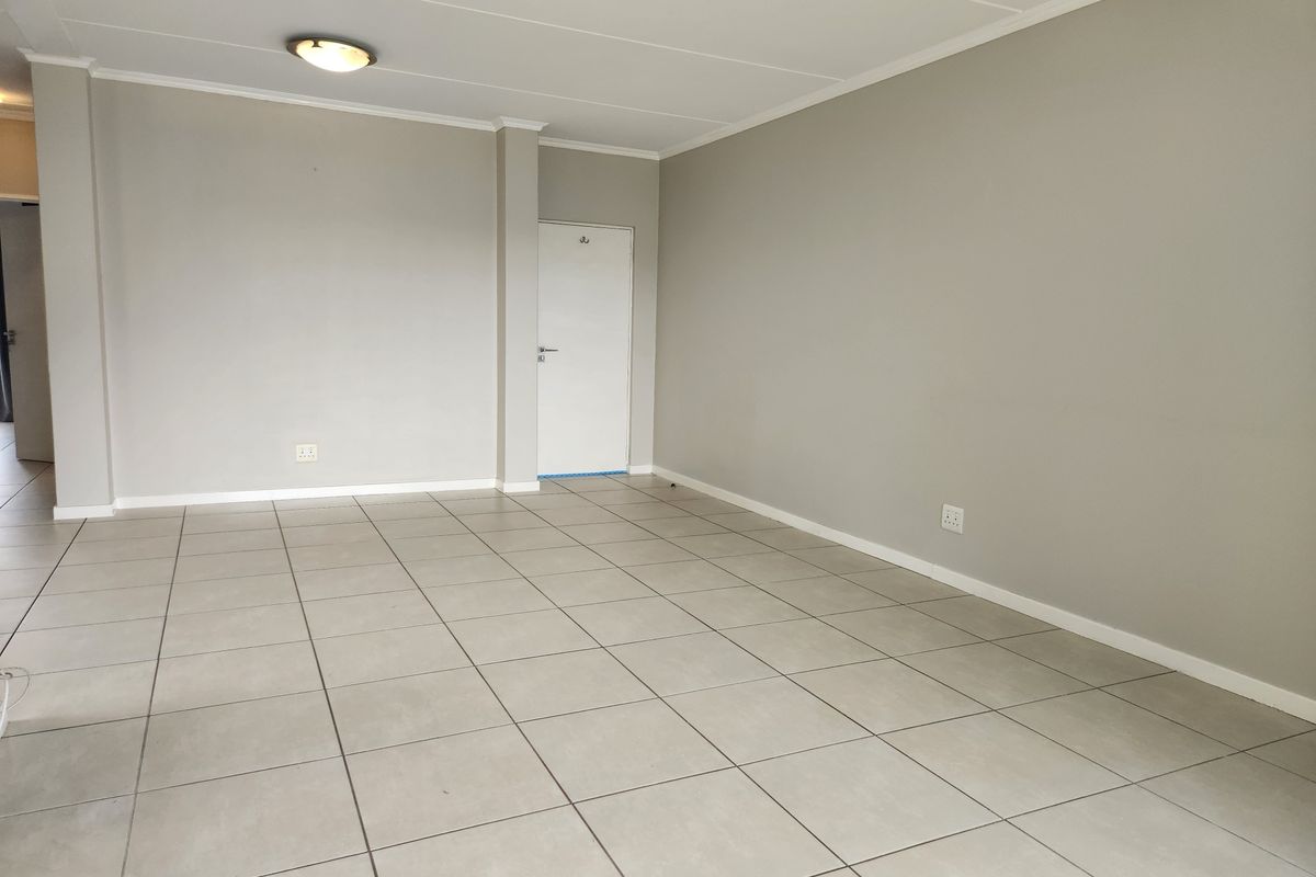 A spacious, empty living area featuring neutral grey walls, tiled flooring, and a simple ceiling-mounted light fixture.