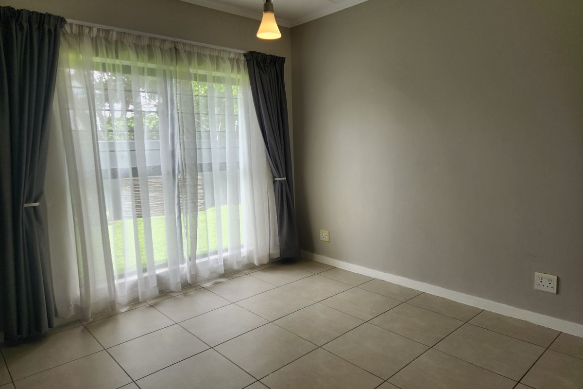 A bright, empty bedroom featuring neutral tiled flooring, a large window with curtain tracks, and a central pendant light fixture.