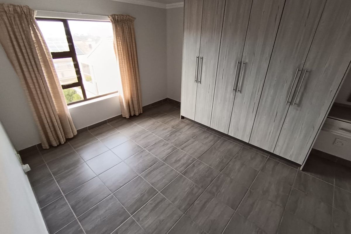 A bright, empty bedroom featuring modern grey wood-look built-in cupboards and neutral tiled flooring, offering a clean and versatile living space.