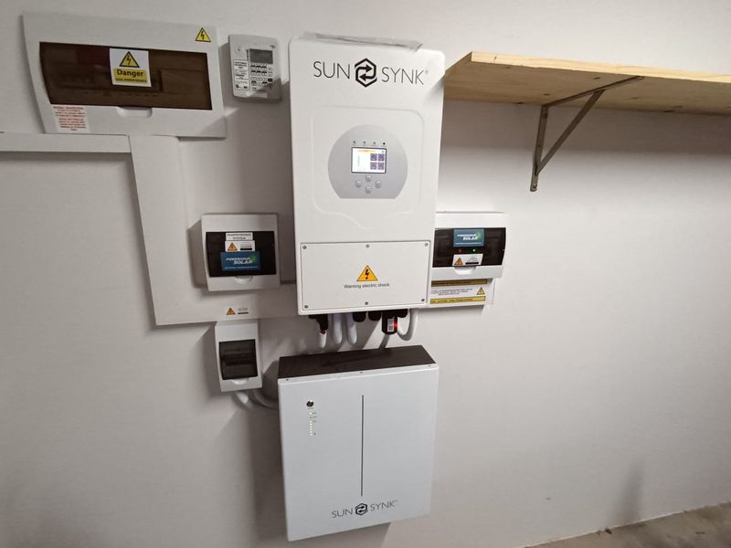 A clean utility area featuring a modern Sunsynk solar inverter and battery storage system, professionally installed with associated electrical distribution components.