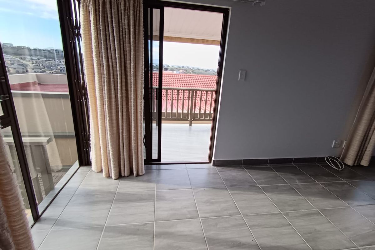 Bright living area featuring large sliding glass doors that open onto a balcony with scenic views and modern tiled flooring.