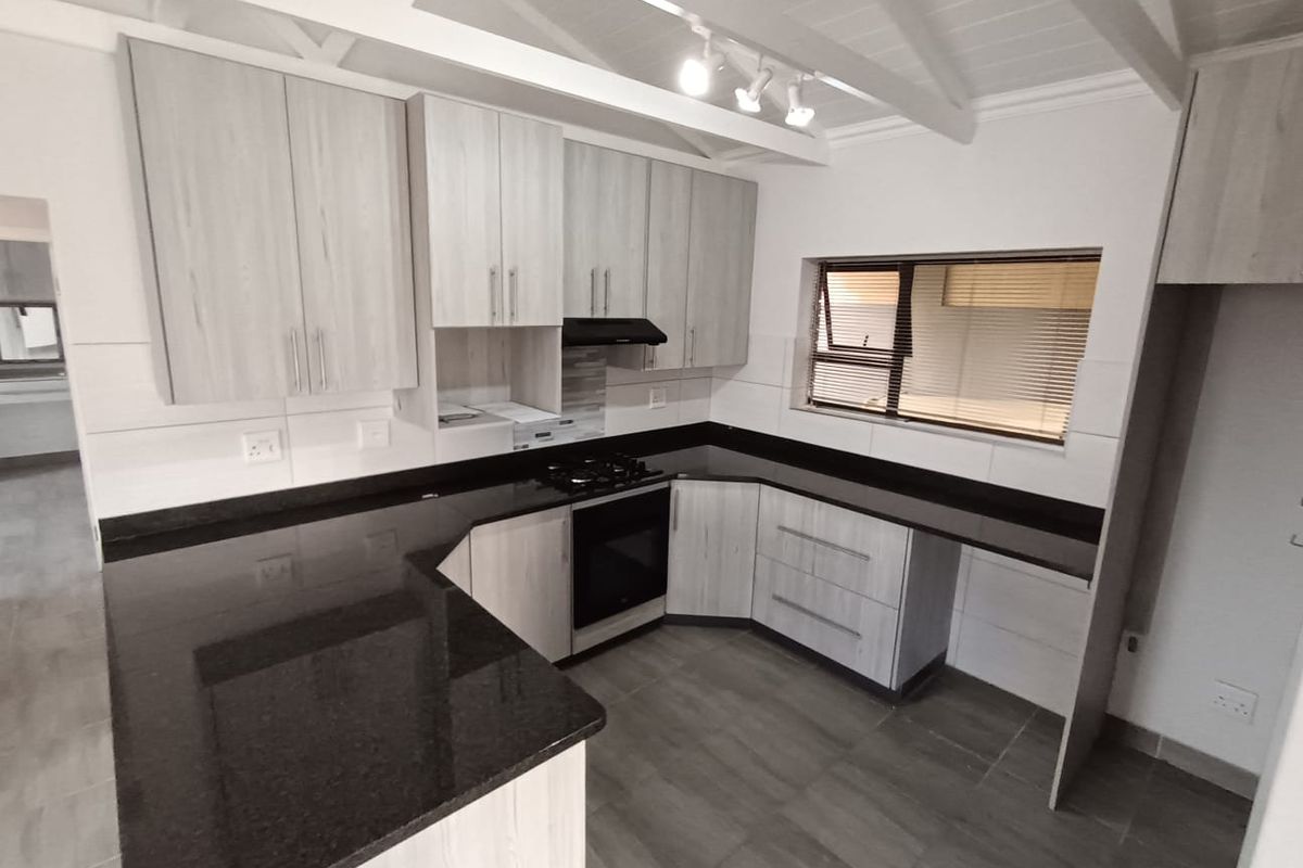 Modern kitchen featuring light wood-grain cabinetry, dark granite countertops, gas hob, electric oven, and exposed beam ceilings with track lighting.