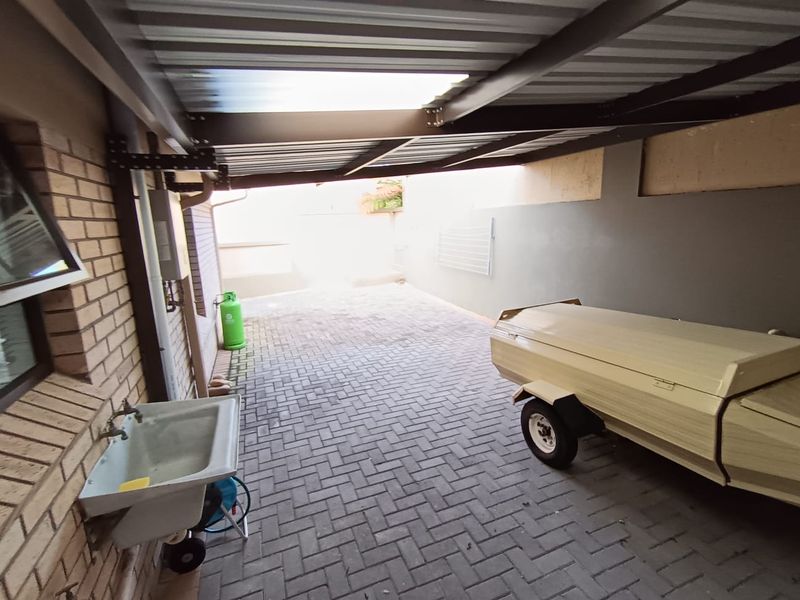 A covered outdoor utility area or carport featuring paved flooring, a wall-mounted utility sink, and a drying rack.