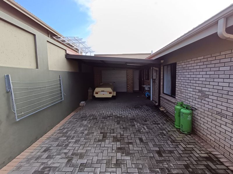 A paved driveway leading to a covered carport and garage, featuring an external utility sink and wall-mounted washing line.