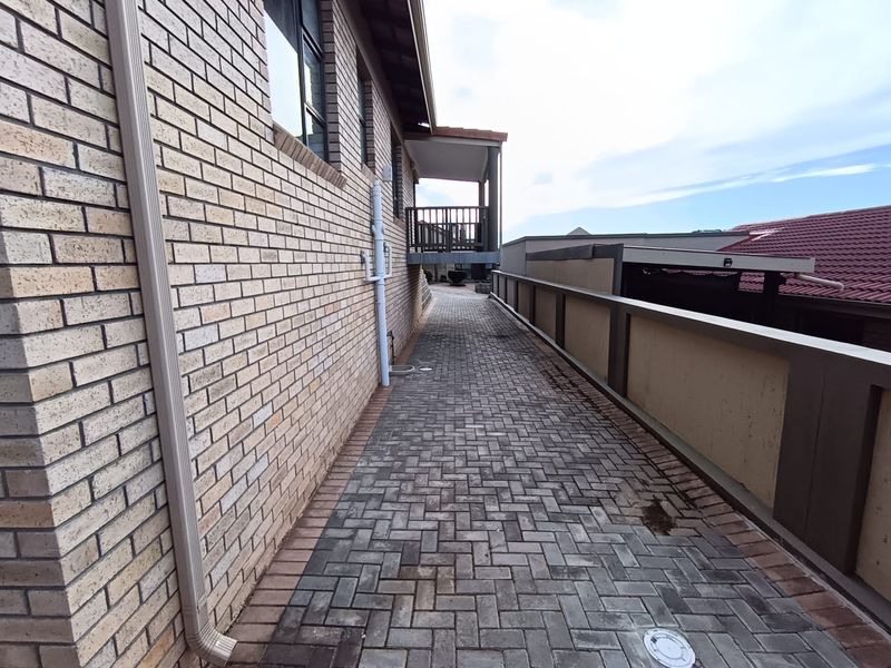 A side exterior walkway featuring brick wall construction, paved flooring, and a view towards an elevated balcony area.