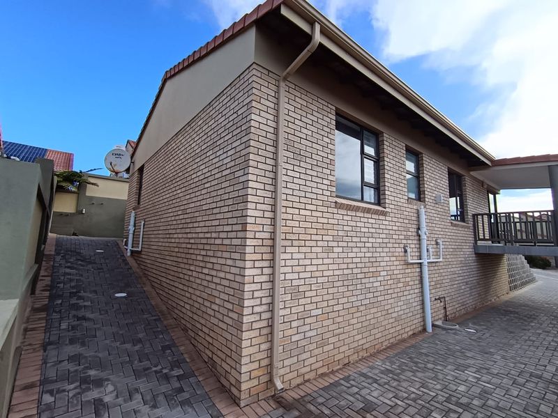 Side and rear view of the townhouse featuring face brick exterior, paved driveway, and aluminium window frames.