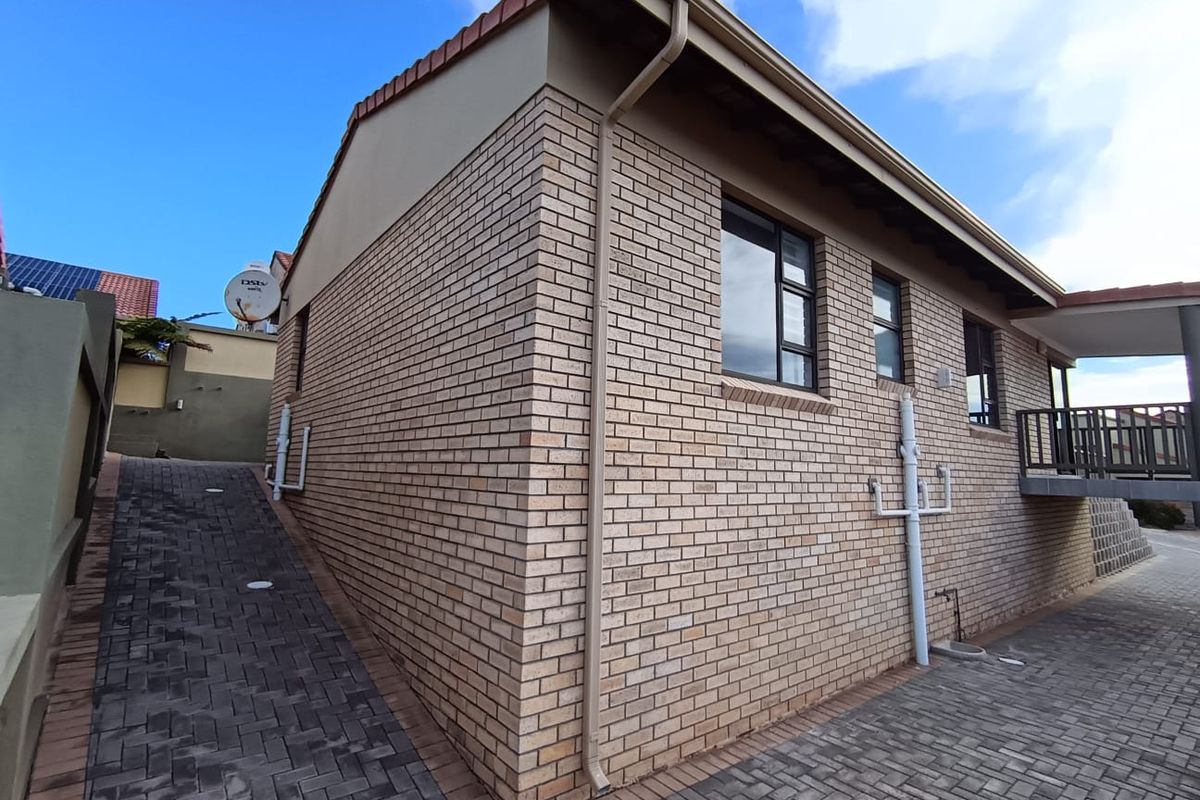 Side and rear view of the townhouse featuring face brick exterior, paved driveway, and aluminium window frames.