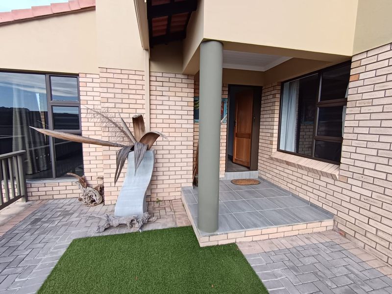 Front entrance of the townhouse featuring a tiled porch, brick facade, and paved exterior area with aluminium window frames.