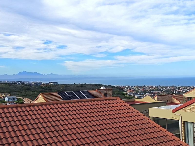 Elevated coastal view overlooking the surrounding neighborhood, rooftops, and distant mountain range, featuring installed solar panels on the roof.