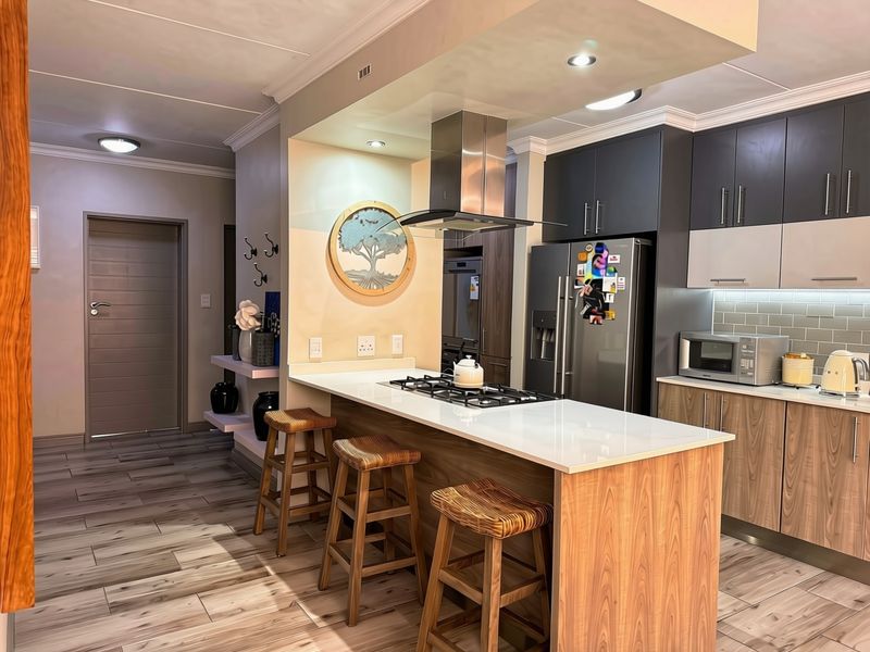 Modern kitchen featuring a central island with gas hob, sleek cabinetry, stone countertops, and contemporary wood-look flooring.