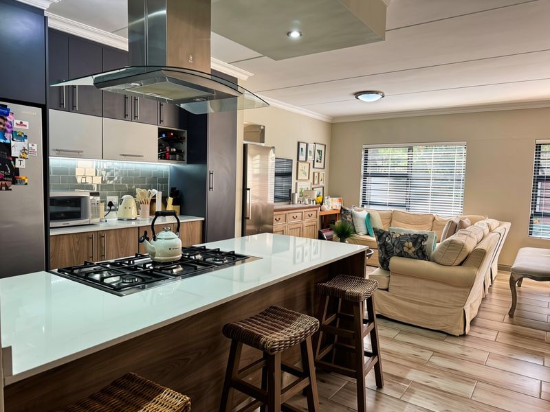 Modern open-plan living area featuring a contemporary kitchen with a central island, gas cooktop, and sleek cabinetry flowing into a comfortable lounge space.