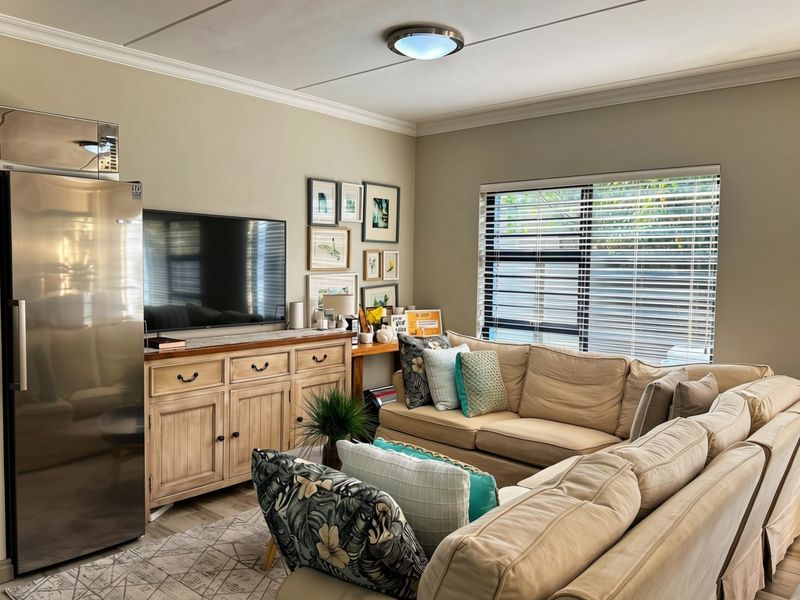 A comfortable living room featuring neutral wall tones, crown molding, and large windows fitted with venetian blinds for adjustable natural light.